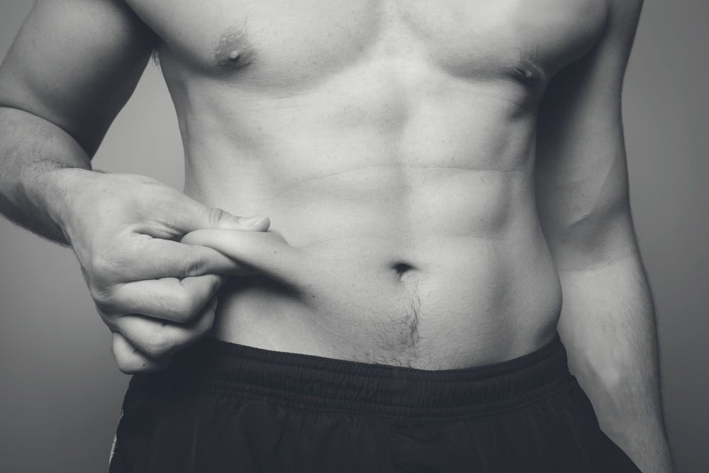 Image of a young man's muscular ab area while he pinches a roll of fat